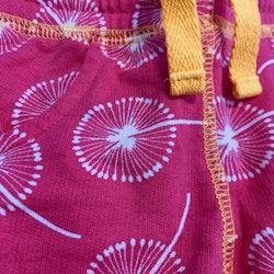 Starkt rosa shorts med vitt maskros mönster och gula detaljer från Maxomorra stl 62/68