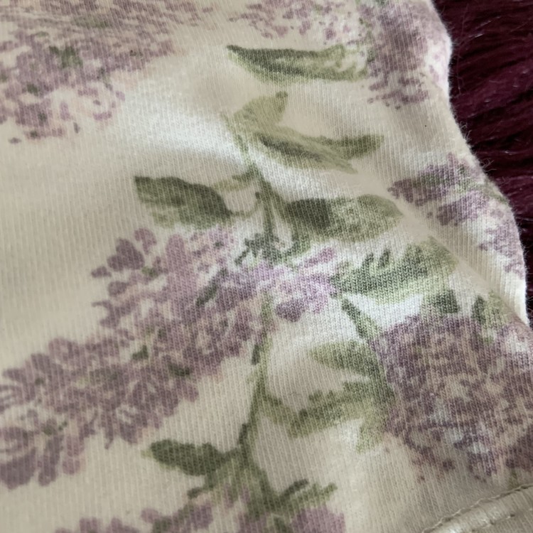 Vit ärmlös body med lila och grönt syren mönster och vita volanger från Newbie stl 56