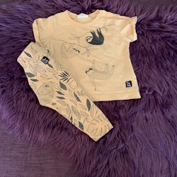 Aprikosfärgat set bestående av en t-shirt med mörkgrått sengångaretryck och leggings med mörkgrått lövmönster från Kaxs stl 68