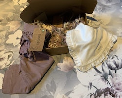 3 delat paket med en lila klänning med djur- och blommönster, lila volangleggings och en vit haklapp från Newbie stl 68 & OS