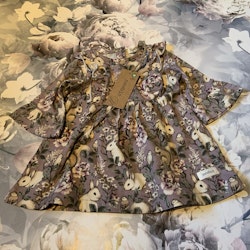 3 delat paket med en lila klänning med djur- och blommönster, lila volangleggings och en vit haklapp från Newbie stl 68 & OS