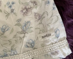 3 delat paket med en vit, blå- och lilablommig volangprydd klänning med matchande solhatt och en haklapp från Newbie stl 62 + 44/46