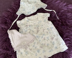 3 delat paket med en vit, blå- och lilablommig volangprydd klänning med matchande solhatt och en haklapp från Newbie stl 62 + 44/46