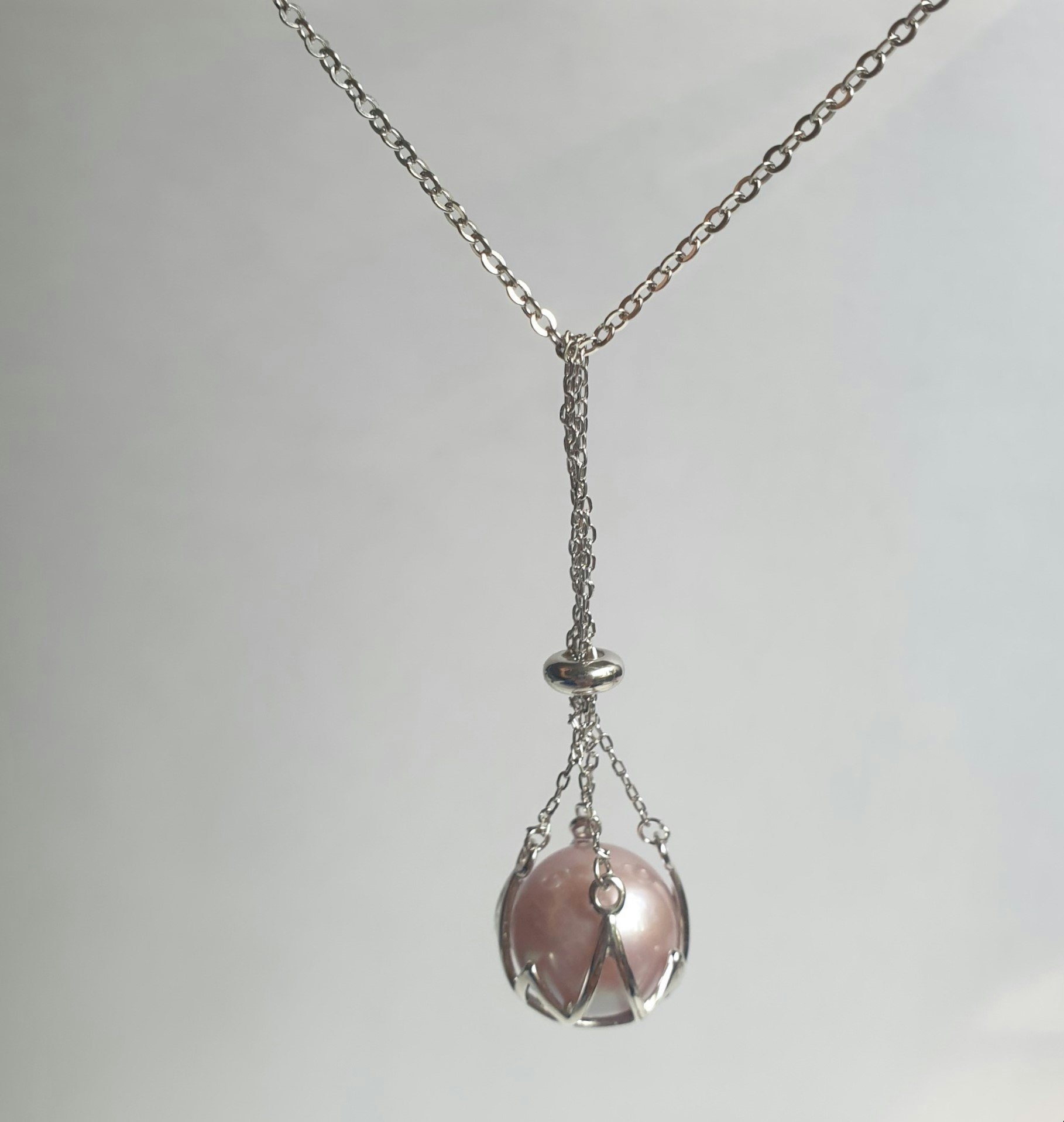En stor rosa pärla i en silverkorg med kedja