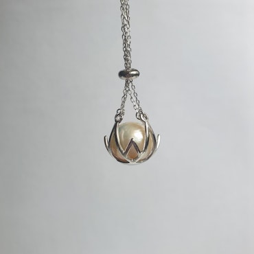 En stor vit pärla i en silverkorg med kedja
