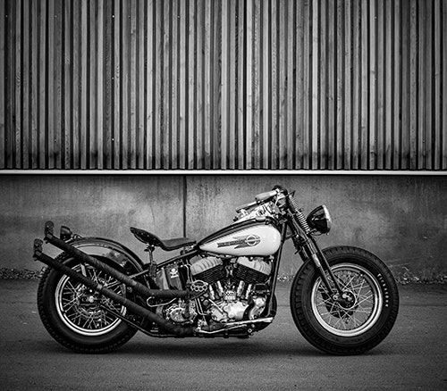 Svartvitt fotografi Harley Davidson vid brädvägg.
