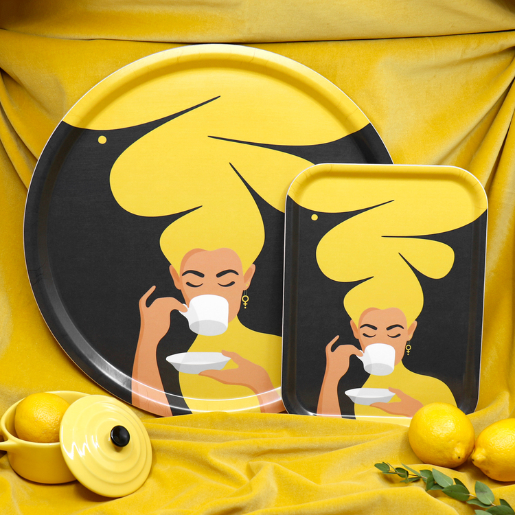 Två brickor – en rund och en rektangulär – med motivet Kaffekvinna i gult. Kaffekvinnan har stort böljande hår, bär ett feministörhänge och njuter av en kopp kaffe.