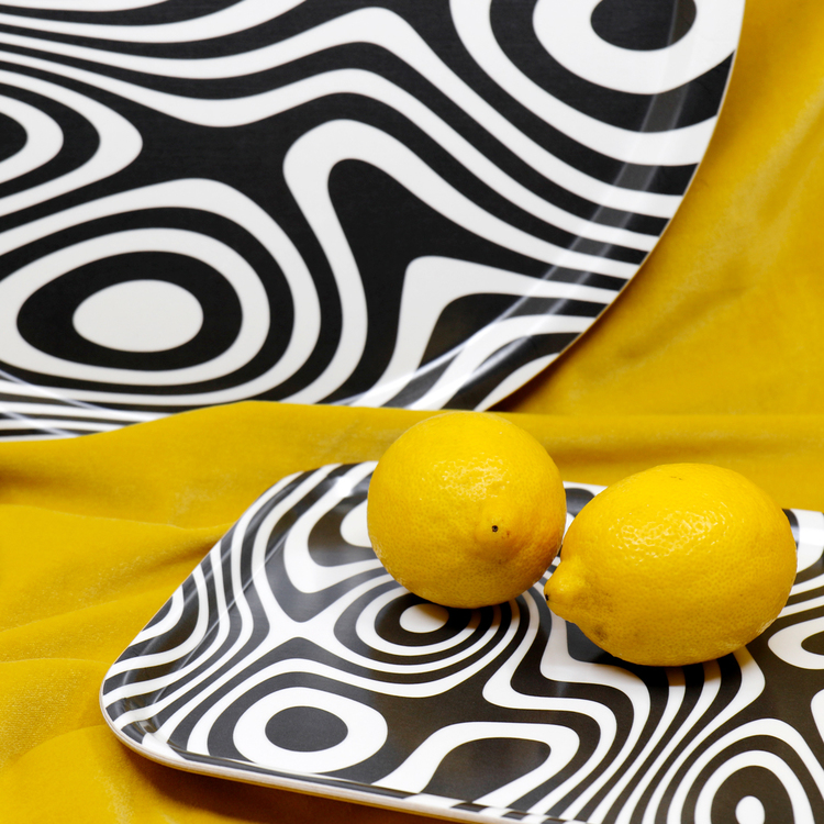 Detaljbild på två brickor och två citroner. Brickorna är svartvita och har ett abstrakt, snurrigt och hypnotiskt mönster.