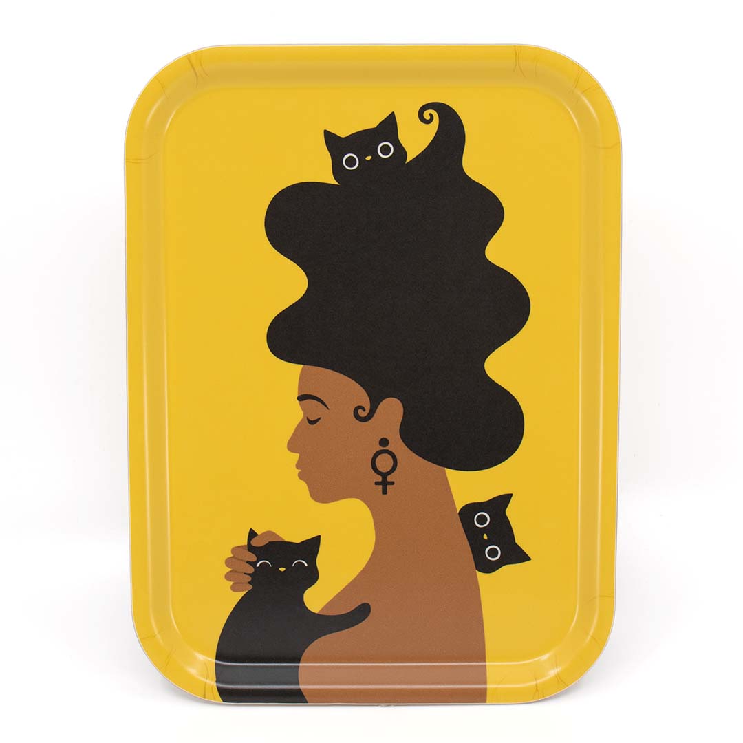 Liten gul bricka med motivet Kattkvinnan – en kvinna med stort böljande hår, en feministsymbol / venussymbol /kvinnosymbol i örat, omgiven av tre busiga katter.