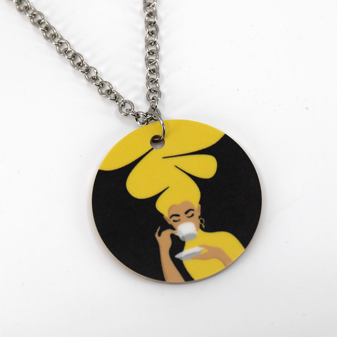 Halsband med motivet Kaffekvinnan – en kvinna med stort bubbligt gult hår som håller i en kaffekopp. Tillverkat av miljömärkt björkfaner.