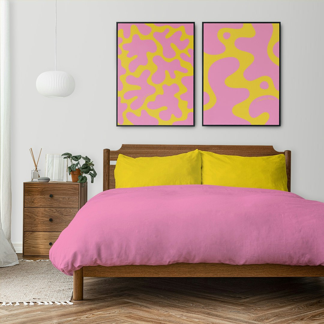 Prints / posters med dom grafiska motiven Blobbar och Kalas. Här ovanför en säng med matchande lakan. Färg: gul och rosa.
