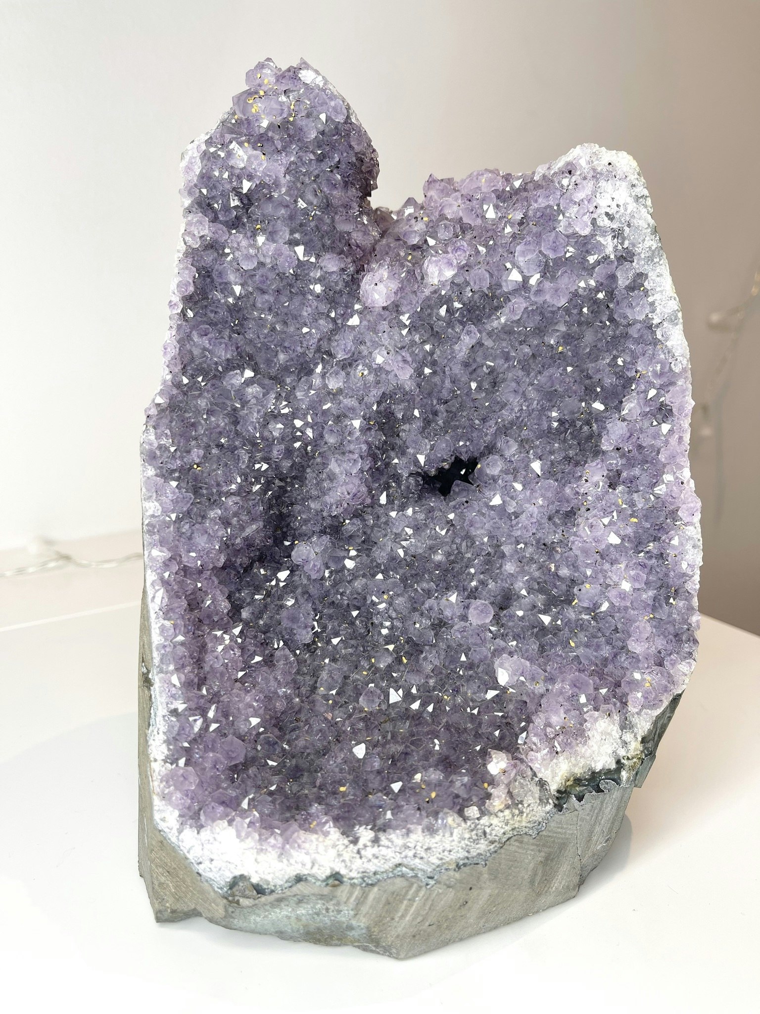 Lila ametistkluster med skimrande kristaller; en naturlig sten som symboliserar inre frid, skydd och healing. Står på en vit bakgrund.