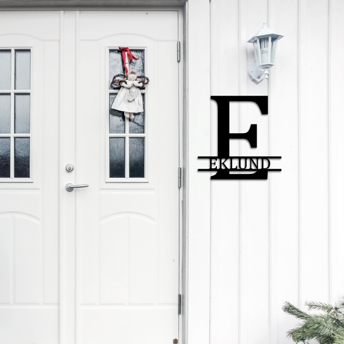 Personligt monogram med namnet Eklund, monterat på väggen bredvid en ytterdörr.