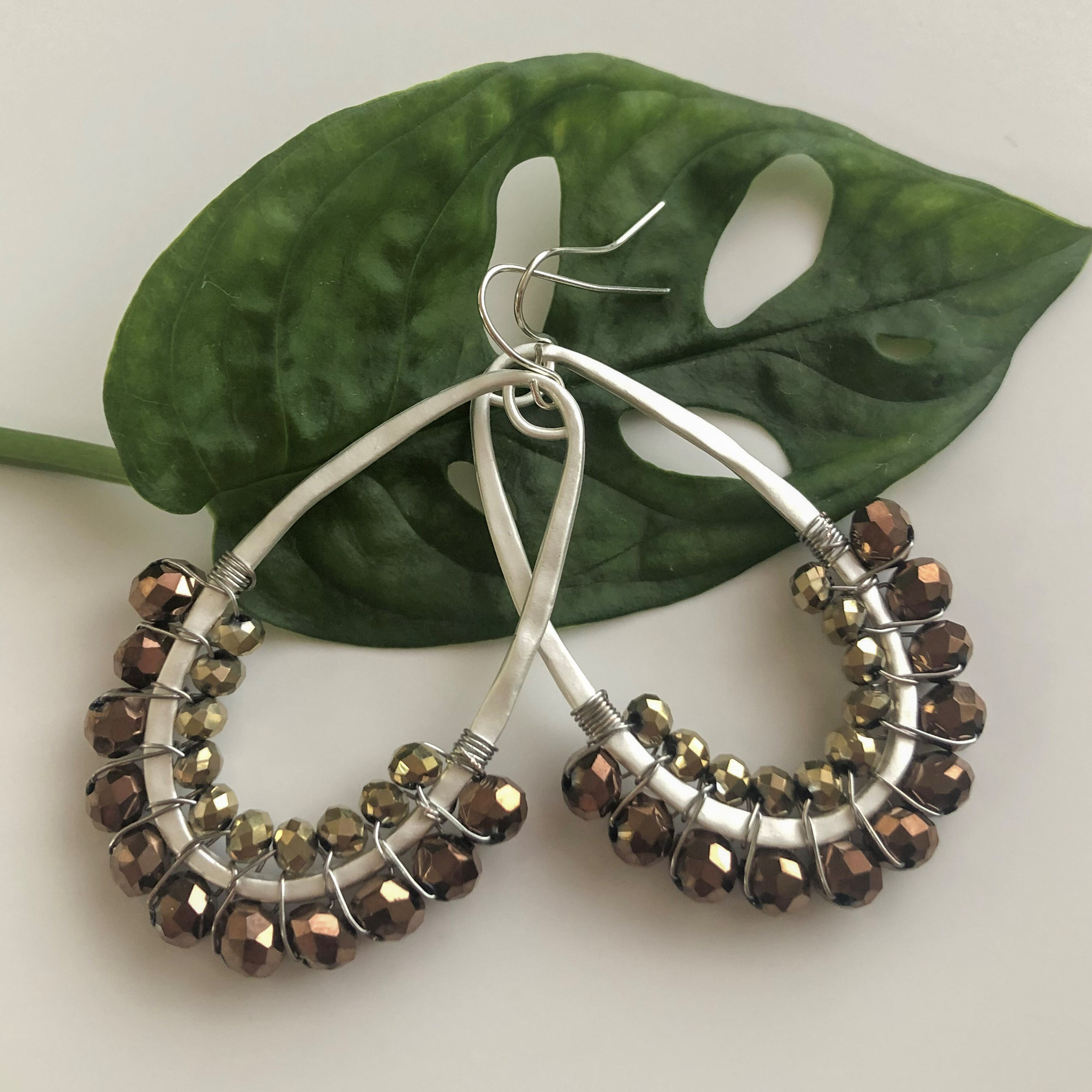 Droppformade handgjorda örhängen i matt silverfärg med bronsfärgade glaskristallpärlor.
