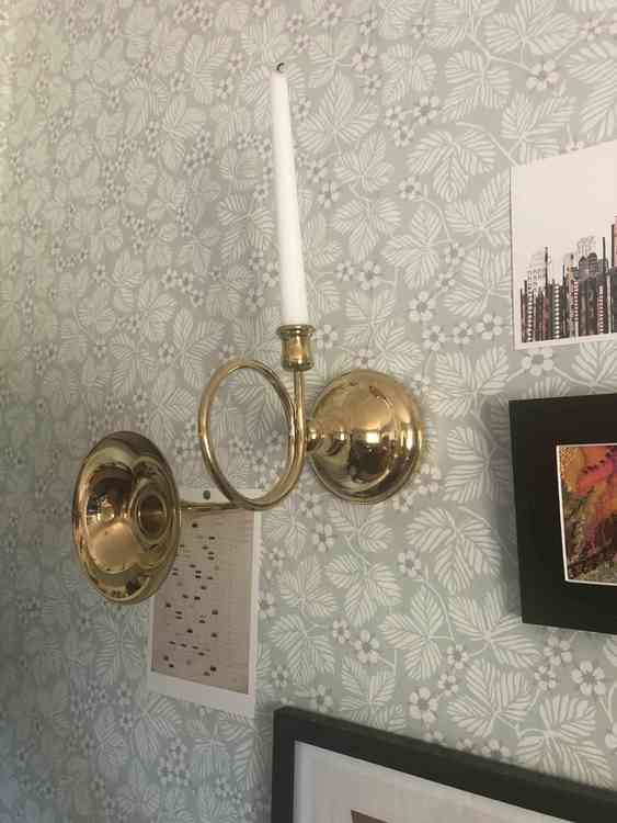Väggljusstake föreställandes ett posthorn i mässing med vitt kronljus monterad på vägg med blommig tapet