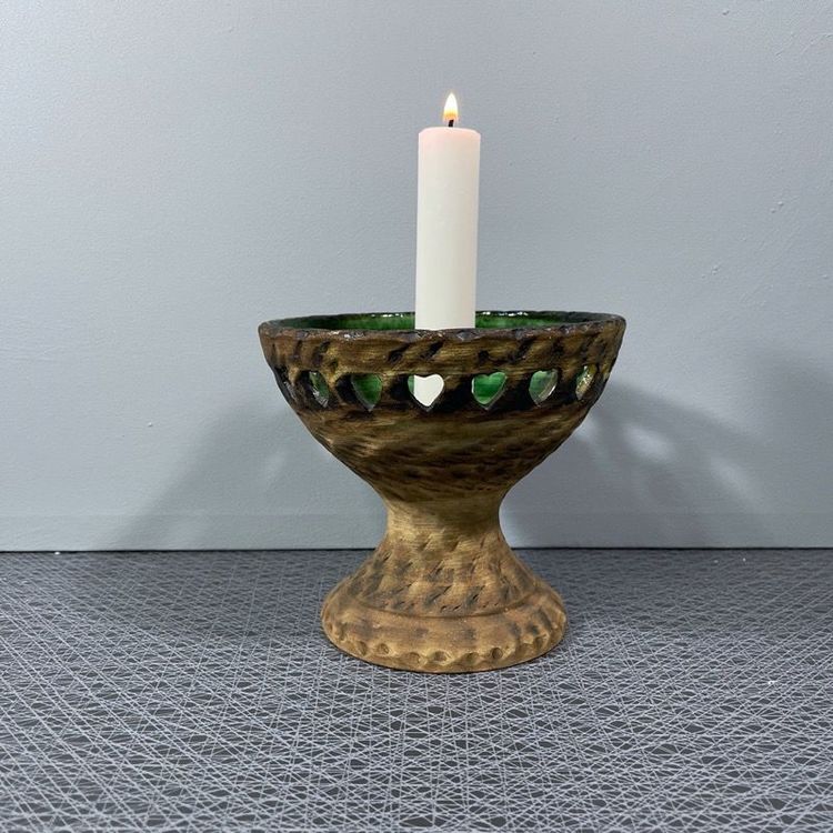 Ljusstake på fot i keramik med grön glasering och perforerad kant med vitt kronljus