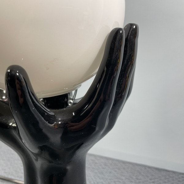 handlampa svart porslin händer som håller en en glaskula närbild glaskula