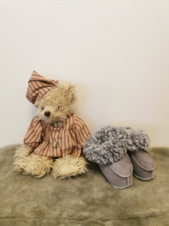 Fin teddybjörn och ett par babytofflor i grå färg
