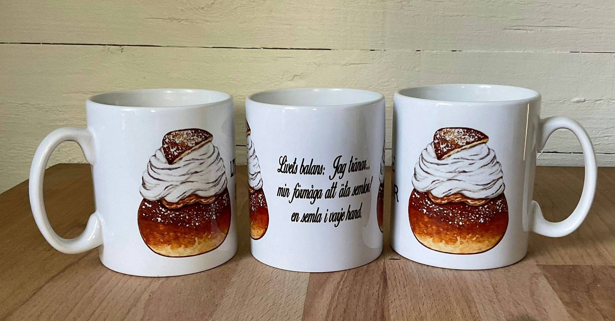 Vit mugg med en bild av en semla och texten Livets balans: en semla i varje hand tryckt på båda sidor, keramik, 330 ml.