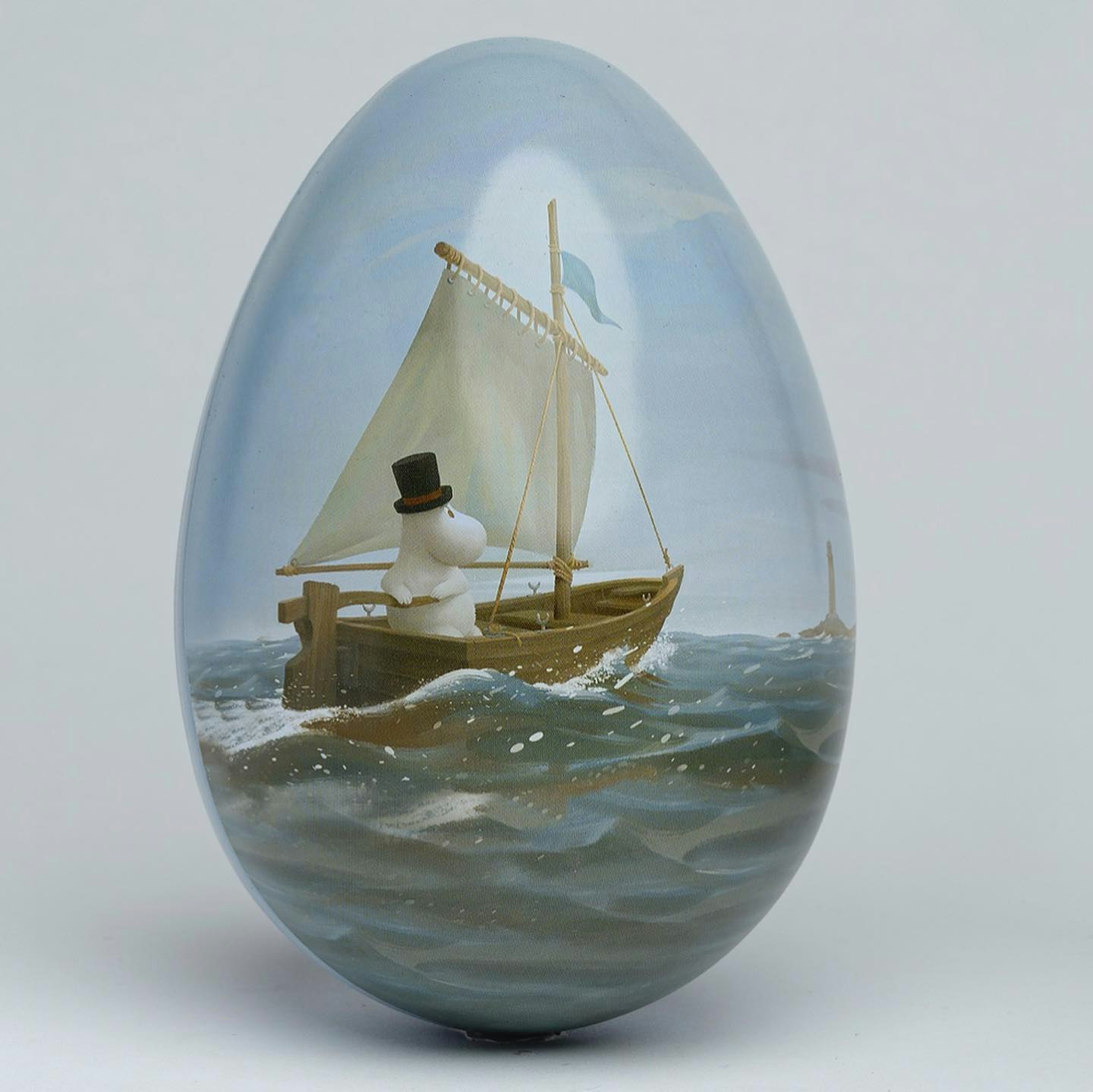 Muminpåskägg i ljusblå färg med motiv av Muminpappan som seglar på havet i en träbåt med vit segelduk.
