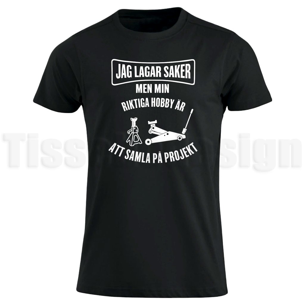 Svart T-shirt med vit text "Jag lagar saker men min riktiga hobby är att samla på projekt", med illustration av domkraft och pallbock