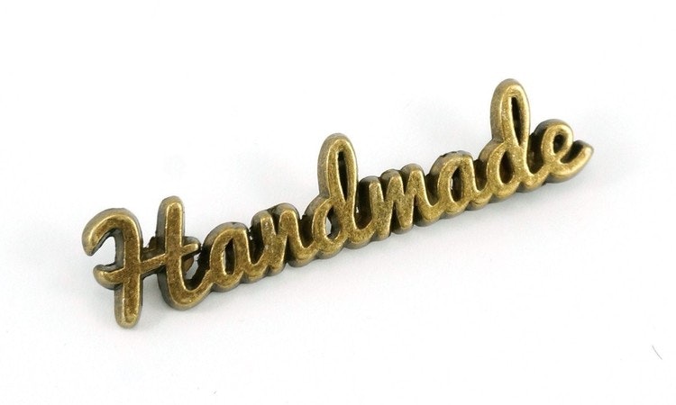 Metal bag label: "handmade", script style