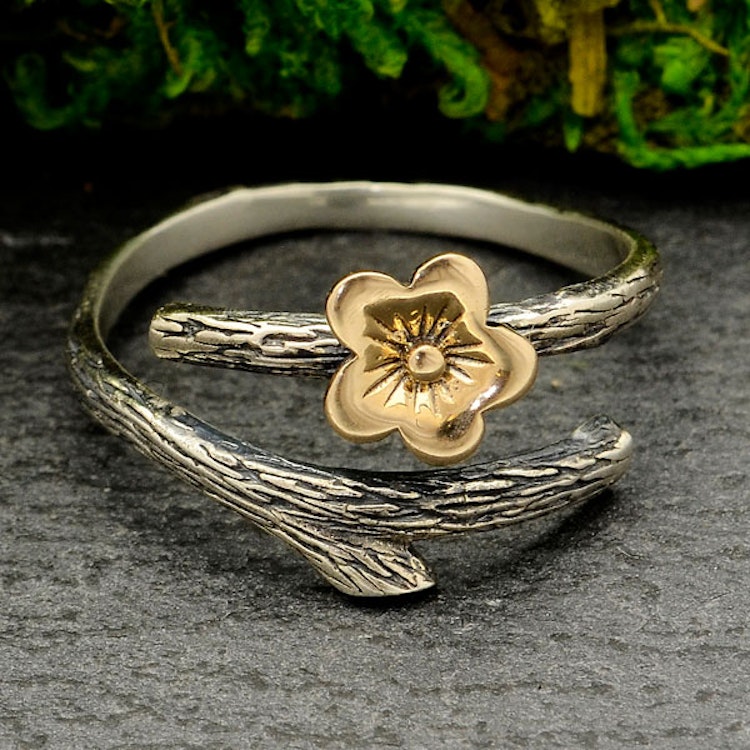 Bilden visar en ring i silver som föreställer en gren med en körsbärsblomma i brons på.