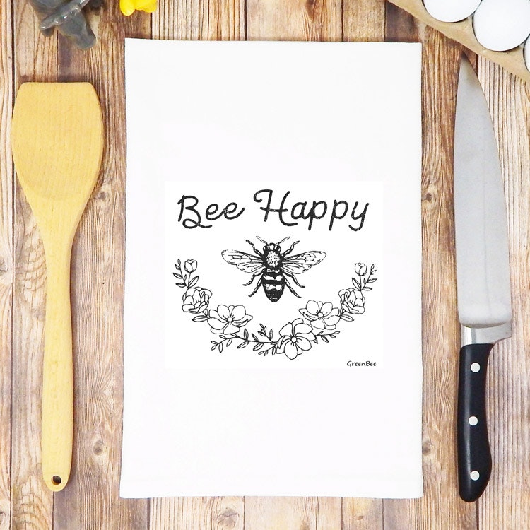 Vit kökshandduk med ett bi samt texten Bee Happy på
