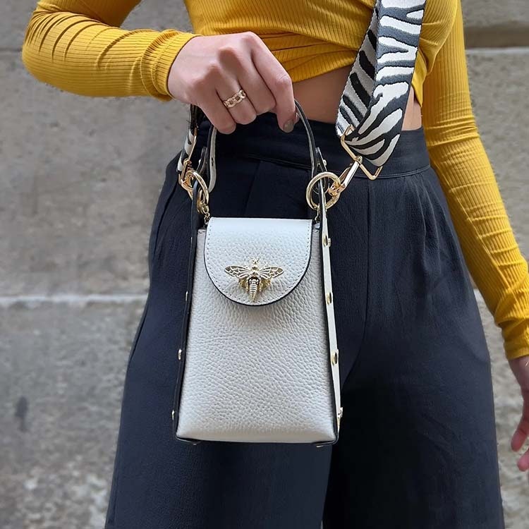Bild på en vit handväska med ett guldfärgat bi som spänne