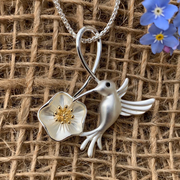 Bild av ett halsband med en hibiskusblomma och en kolibri i matta silvertoner