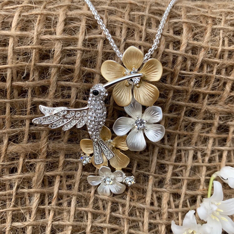 Bild av ett halsband med blommor i guld och silvertoner samt en gnistrande kolibri