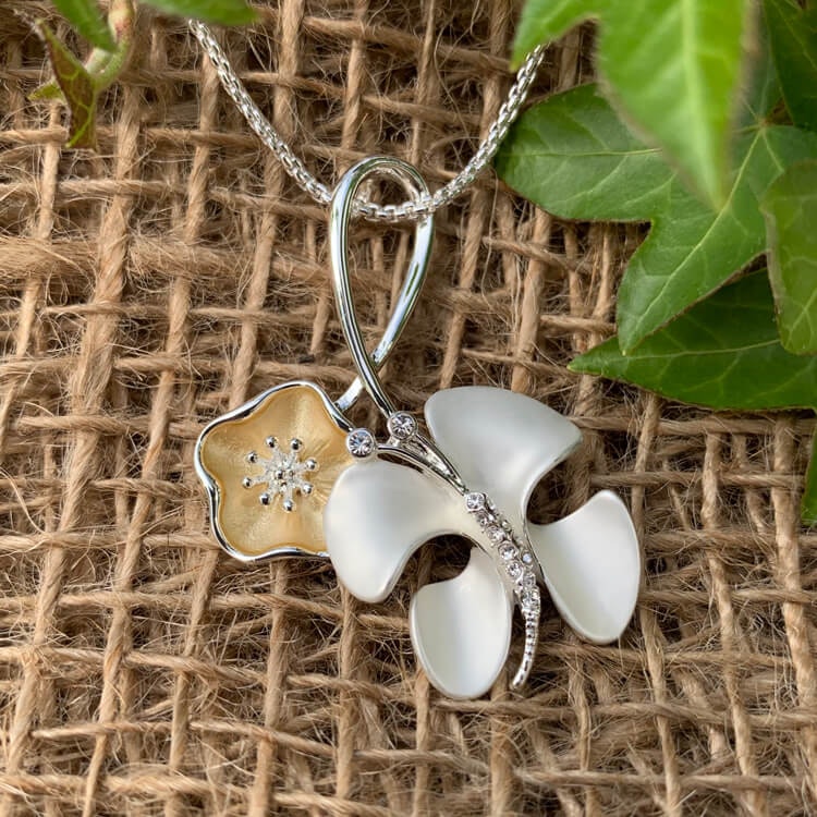 Bild av ett halsband med en abstrakt fjäril samt en blomma i silver- och guldtoner