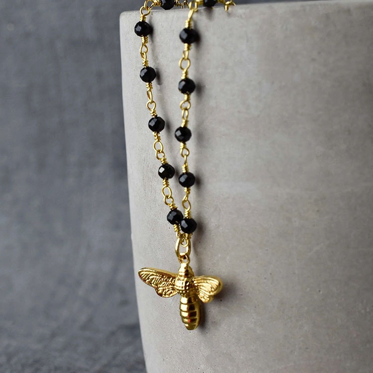 Bild på ett halsband som består av en guldfärgad kedja med svarta onyxer på samt ett guldfärgat bi i centrum.