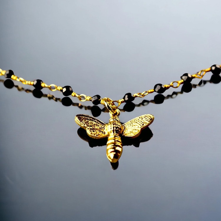 Bild på ett armband med ett guldfärgat bi samt med en kedja med onyxer