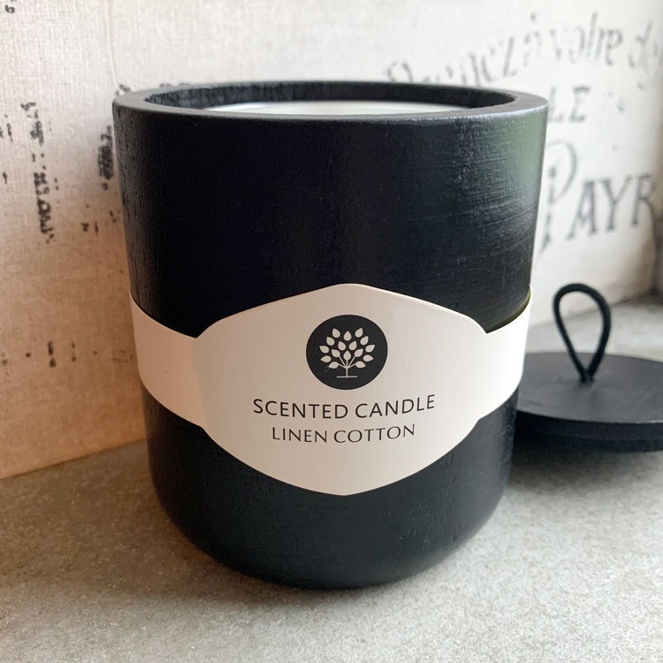 Bild på ett doftljus med doften linen cotton. Ljushållaren är tillverkad i svart trä.