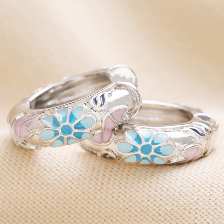 Bild på ett par silverörhängen i form av breda ringar med blommönster i blått och rosa.