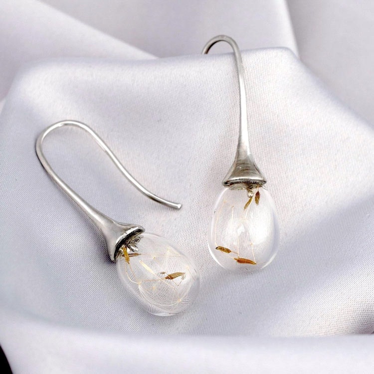 Bild som visar ett par silverpläterade örhängen med torkade maskrosfrön i glasdroppar