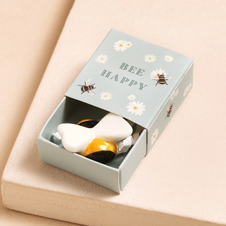 Bild på en liten lyckomaskott i form av ett keramikbi i en ask med texten "Bee Happy"