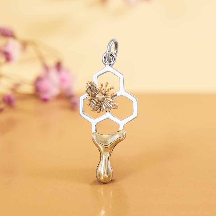 Bild på ett silverhänge som föreställer en vaxkaka med ett litet bi samt droppande honung i brons