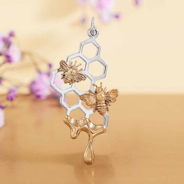 Bild på ett hänge som föreställer en vaxkaka i silver med två bin samt droppande honung i brons