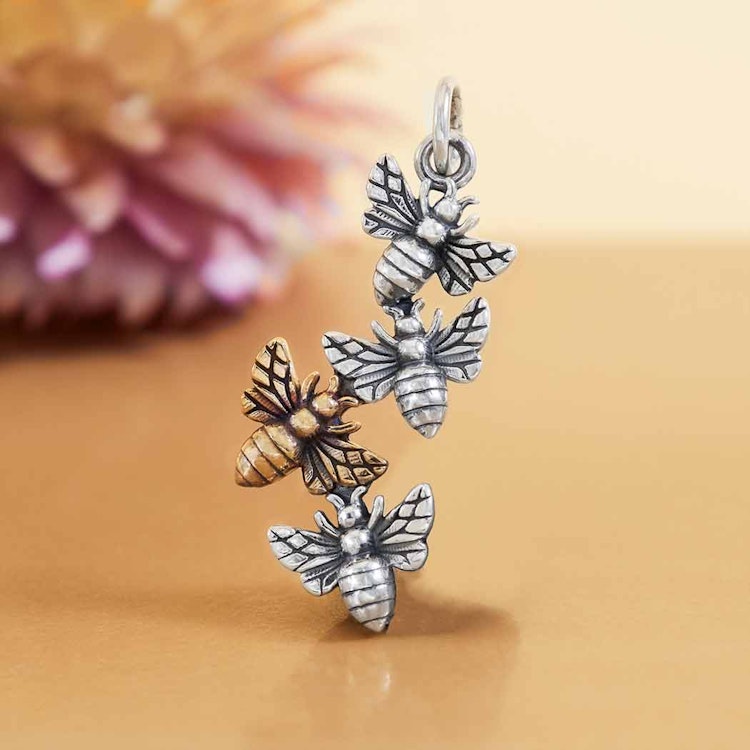 Bild på ett hänge med tre bin i silver samt ett bi i brons.