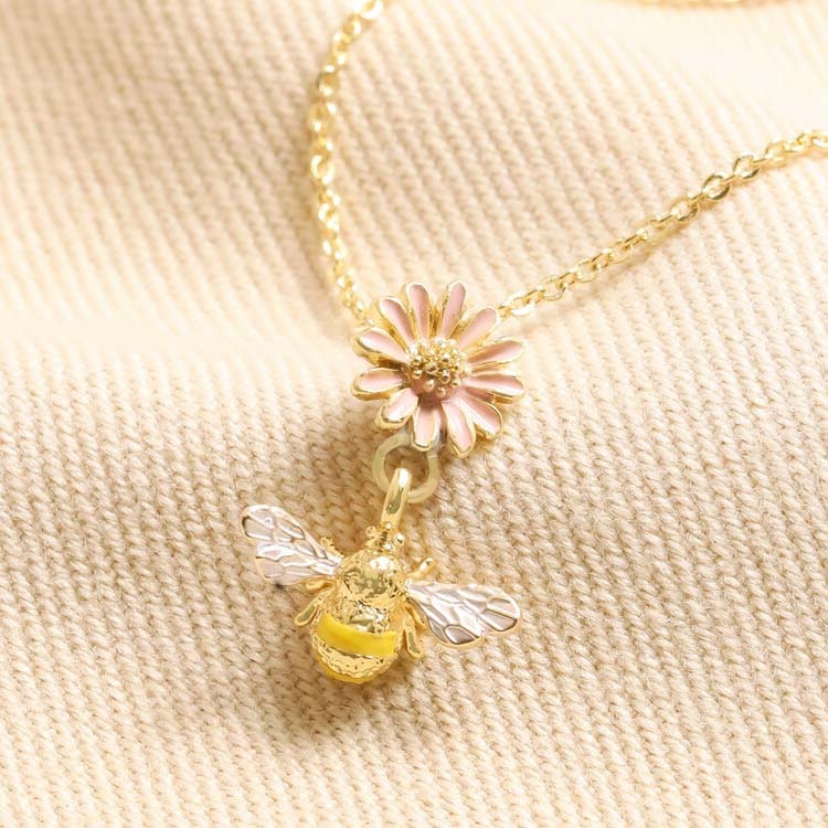 Bild som visar ett guldpläterat halsband med en pastellrosa blomma samt ett gult litet bi.