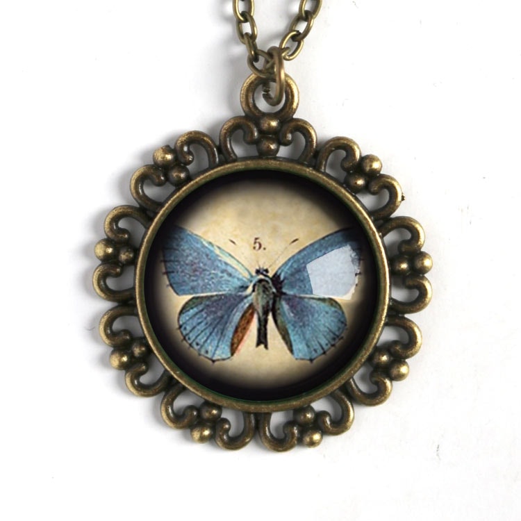 Bild som visar ett vintageinspirerat halsband i mässing med en illustration av en blå fjäril.
