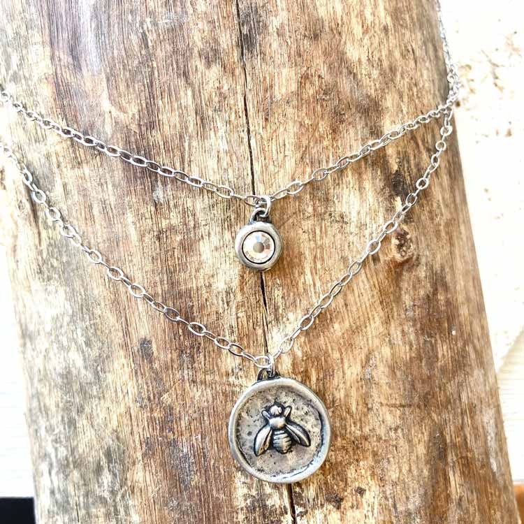 Bild som visar ett halsband med dubbla kedjor och hängen. Ett med ett bi och en kristall