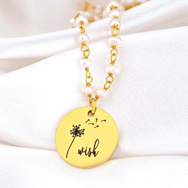 Bild på ett halsband med sötvattenspärlor och ett hänge med texten Wish samt maskrosfrön