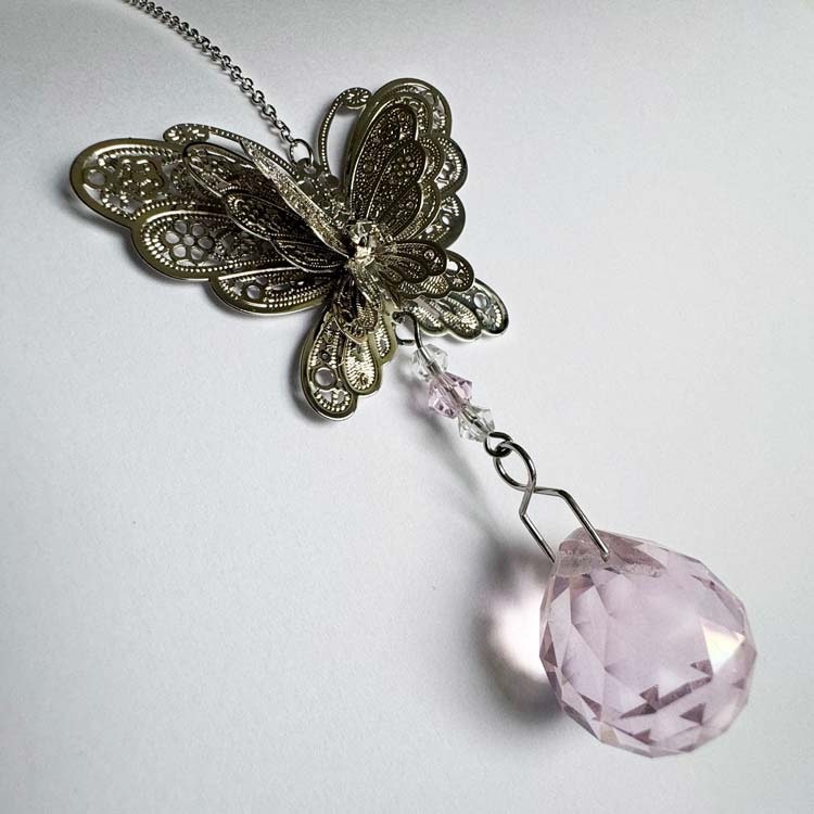 Solfångare med silverfärgad fjäril och rosa prisma.