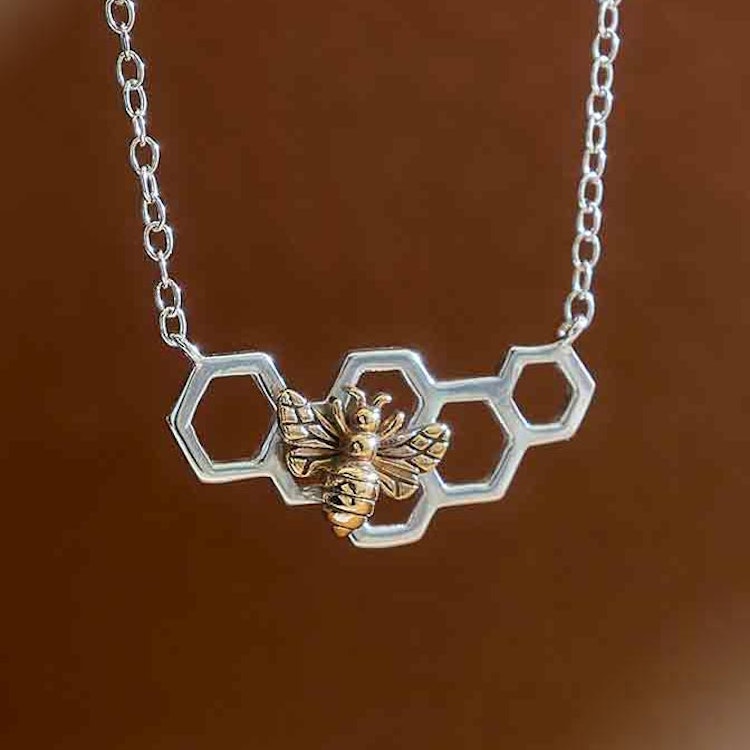 Bild som visar ett silverhalsband som föreställer en liten bit vaxkaka med ett bronsbi på.
