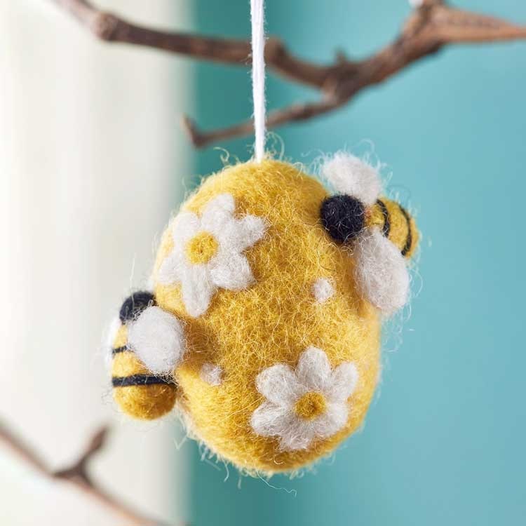 Bild på ett tovat ägg med blommönster samt två bin. Perfekt påskpynt.