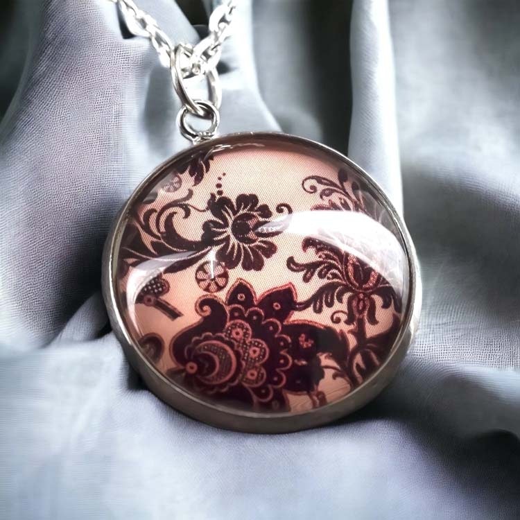 Halsband med blomstermotiv på rosa bakgrund under en cabochon av glas.