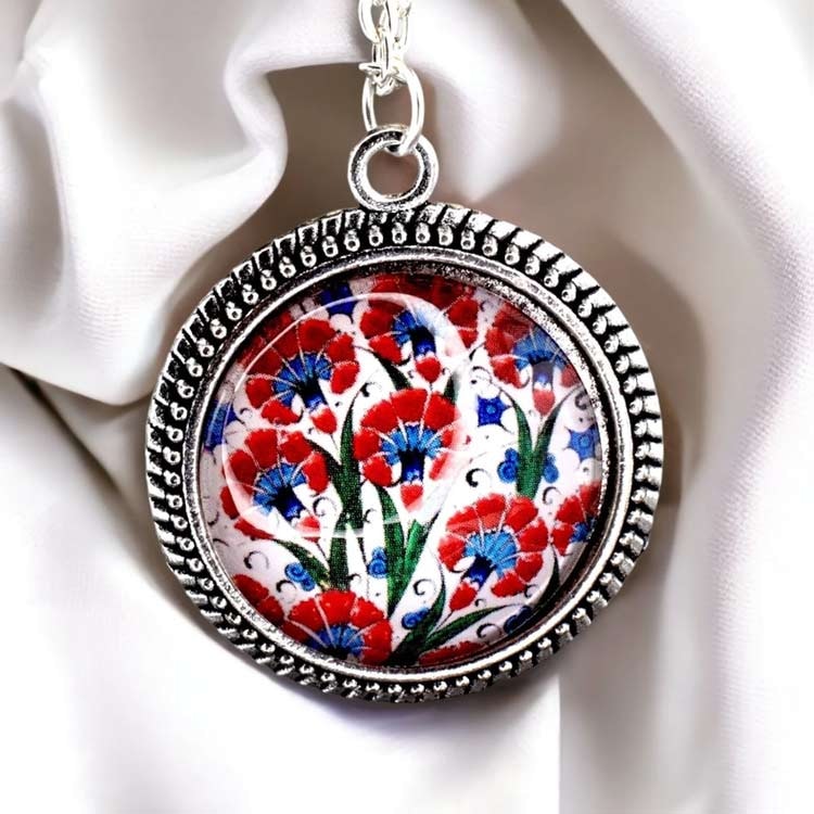 Silverpläterat halsband med färgstarkt blommotiv under en cabochon av glas.